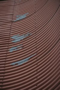 A homeowner examines curled shingles and a water stain beneath a residential roof during a daylight inspection.